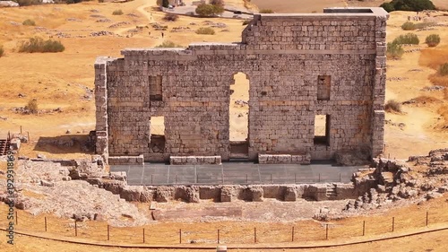 Cinematic 4K drone shot of the ancient Roman theater of Acinipo archaeological site, showing the standing stone wall and seating area in the mountains near Ronda, Malaga province.