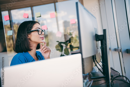 Photos Businesswoman at a computer in a bright office thinks deeply while sticky notes