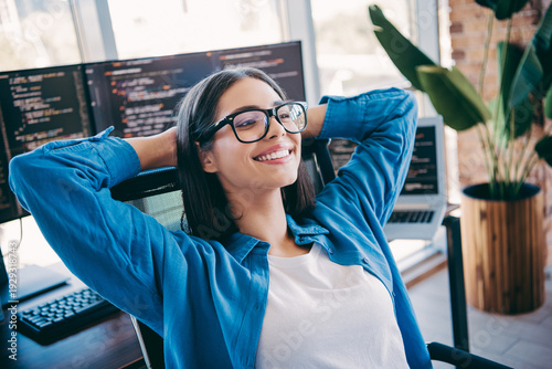 Φωτογραφία Happy female programmer in a modern loft office coding at desk with multiple mon