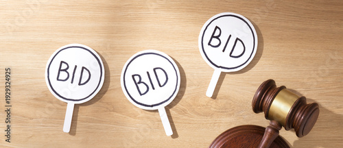 Foto Wooden gavel on sound block next to multiple white BID signs on a wooden desk, symbolizing auction bidding and competitive sales