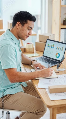Man working at desk reviewing data on laptop with boxes in background