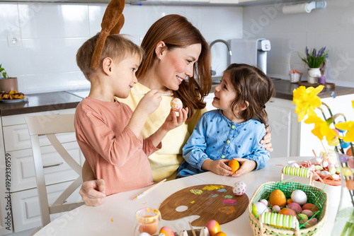 Fotografía Smiling Mother Painting Easter Eggs with Two Children at Home