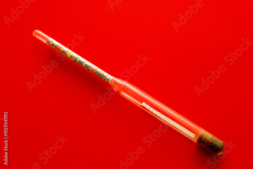 Photography A glass hydrometer with a colored scale is positioned diagonally on a rich red background
