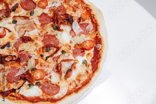 Close-up of pepperoni pizza with melted cheese, cherry tomatoes and capers on thin crust