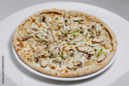 White pizza with mushrooms and sliced chicken on a plate, melted cheese and herbs
