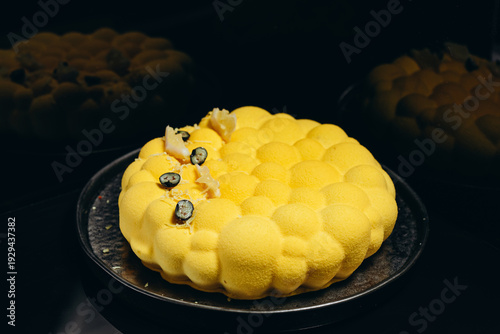 Yellow mousse cake with bubble texture and blueberry garnish on black plate, modern dessert presentation