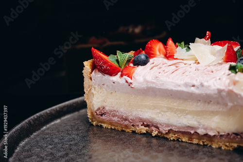Slice of strawberry cheesecake with cream layers and fresh berries on dark plate