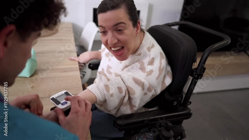 Male caregiver checking the blood pressure of a happy woman with a disability sitting in a motorized wheelchair, capturing a moment of positive healthcare interaction and assisted living