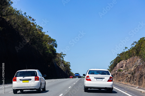 sunlit cars traveling on road cut through mountain rock in NSW Australia