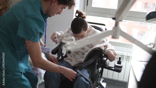 Supportive male caregiver helping a smiling woman with a disability, securing her in a motorized wheelchair at home. Empathy and compassionate assistance from a dedicated healthcare professional