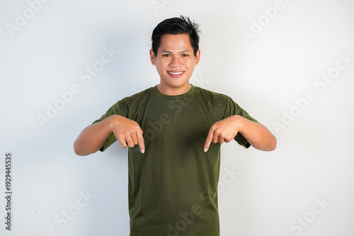 Smiling young Asian man wearing a green shirt points down