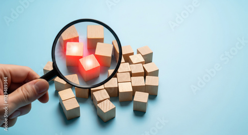A hand holding a magnifying glass over glowing red cubes, perfect for identifying problems and focused business analysis plans
