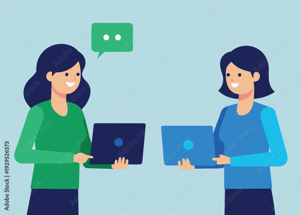 Fototapeta premium Two smiling businesswomen standing and holding laptops, with a chat bubble indicating communication.