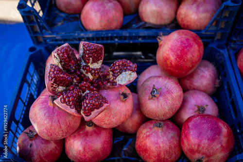 Fresh pomegranates displayed in a market crate with one cut open showing red seeds. Organic fruit at farmers market