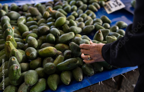Woman selecting fresh organic avocados at a local farmers market