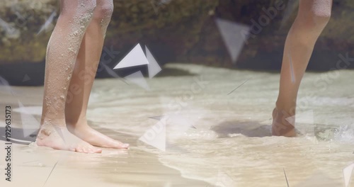 Two girls playing lifting foot creating splash toward feet, triangles drifting over feet for design