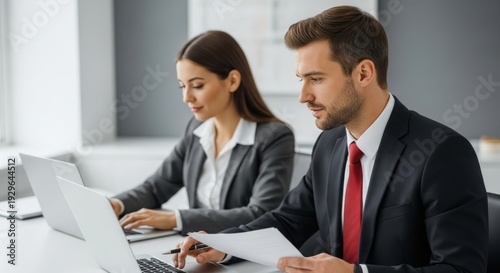 Professionals collaborating on laptops in an office setting while reviewing documents