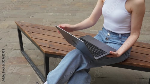 Person working on laptop while sitting on bench outdoors in urban area during daytime