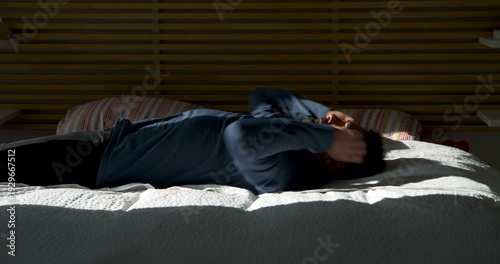 Despondent Serenity: A lone individual finds solace in solitude, laying prone on a soft bed as shadows dance across the room, encapsulating feelings of melancholy and introspection.