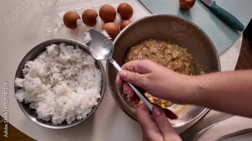 A woman cooks meatballs. A woman adds boiled rice to a metal bowl with minced meat
