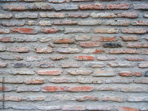 A wall made of about 60 old brown bricks with jagged edges, held together with grey cement.