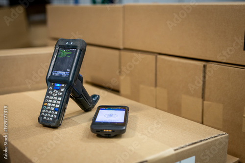 Two different types of warehouse RFT terminals and barcode scanners placed on a cardboard box in the warehouse