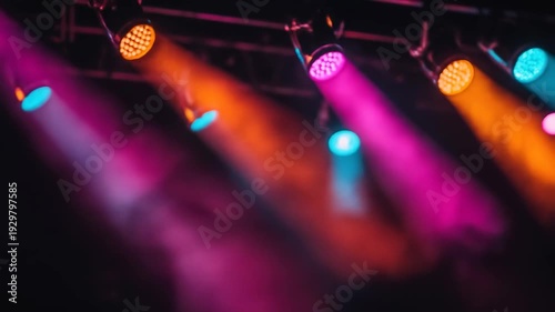 Vibrant stage lights cast intersecting beams of orange, pink, and blue light in darkness