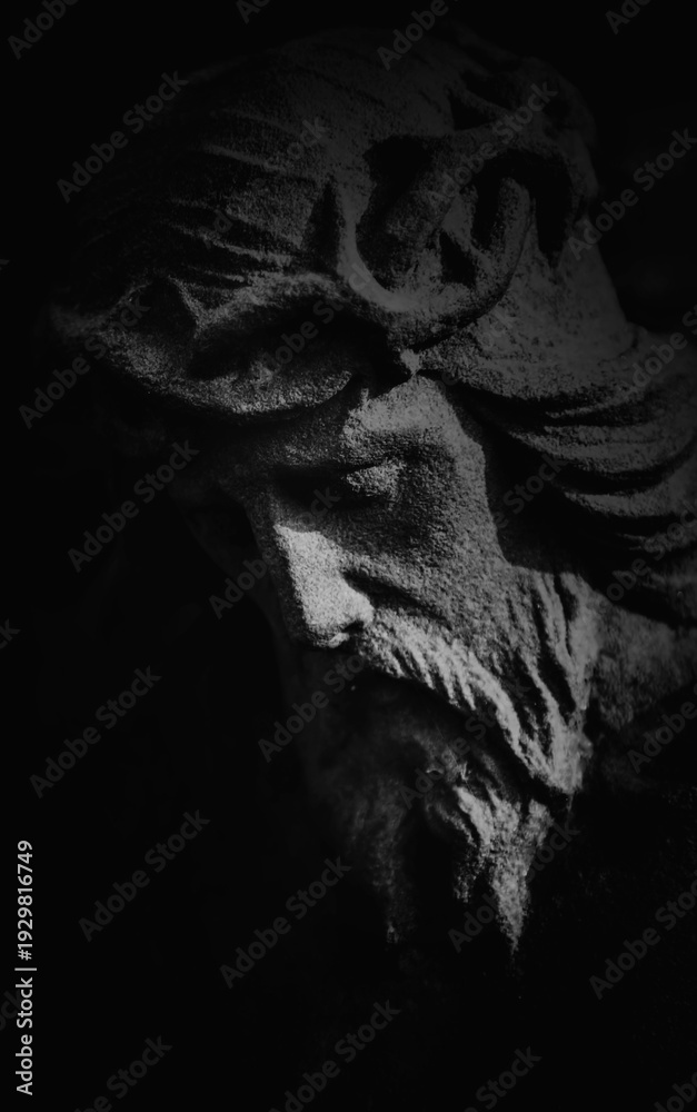 Naklejka premium Dark dramatic close-up of Jesus Christ stone statue in deep shadow, symbol of suffering, sacrifice, faith, and spiritual endurance.