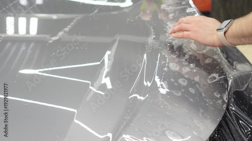 A car wrapping specialist applies a polyurethane film to the car. Detailer smoothes PPF. Car wrapping, detailing, tuning and styling. PPF protective film against chips and scratches. Car protection.