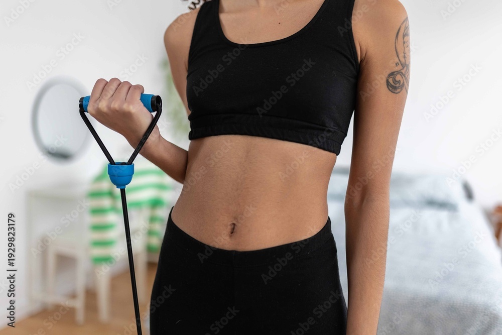 Naklejka premium Young woman exercising her arm with a resistance band at home, focusing on her fitness and well-being