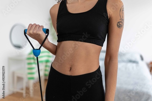 Young woman exercising her arm with a resistance band at home, focusing on her fitness and well-being