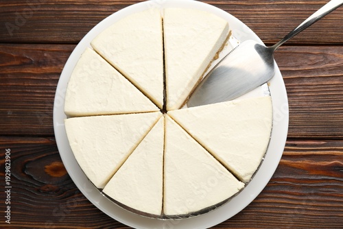 Tasty cut cheesecake and server on wooden table, top view