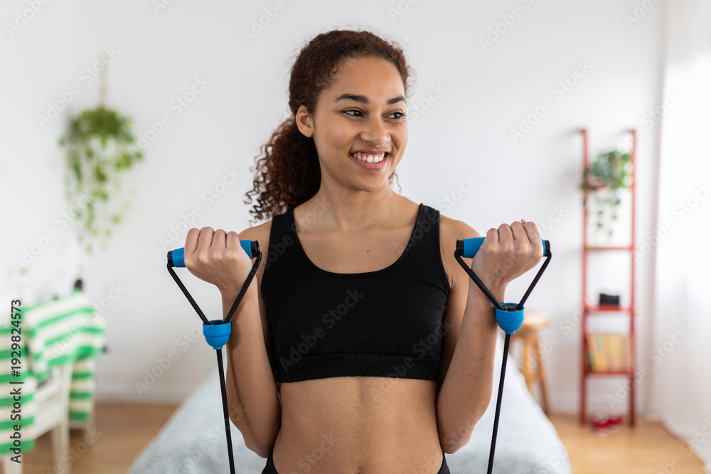 Obraz premium Happy Latin woman exercising with elastic resistance band at home, enjoying her workout routine