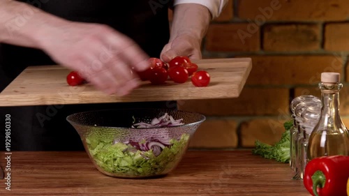 The cook cuts the tomatoes into halves for the salad with a knife and places them in a bowl.