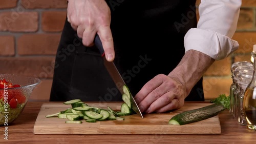 A cook cuts cucumber into pieces for a salad with a knife.