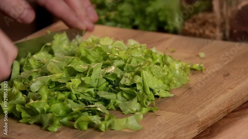 A male chef cuts green salad leaves with a knife on a cutting board.