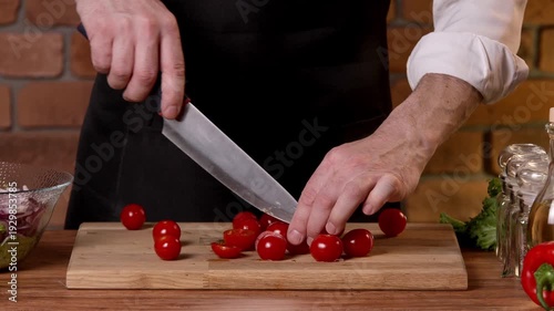 A chef cuts tomatoes into halves for a salad on a cutting board with a knife.