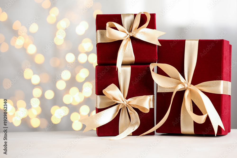 Fototapeta premium Red gift boxes on white table against blurred bokeh lights, closeup. Space for text
