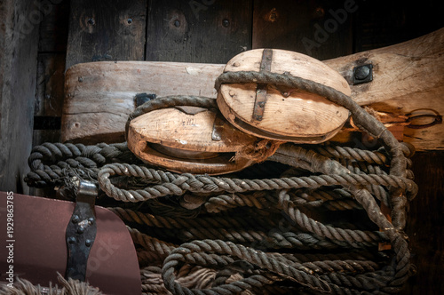 A collection of wooden blocks and thick ropes lie intertwined on a wooden surface. These elements depict the intricate components of ship rigging.