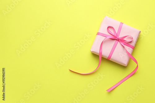 One pink gift box on yellowish green background, top view. Space for text