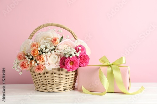 Beautiful flowers in basket and gift on white wooden table. Space for text