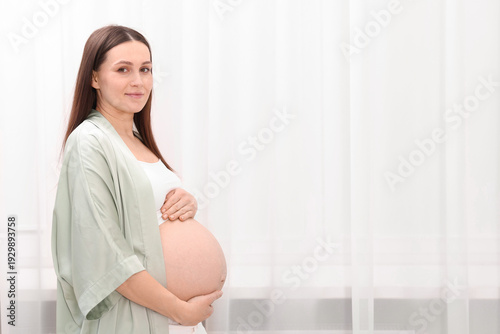 Beautiful pregnant woman touching her belly near curtains at home, space for text Free Download Beautiful pregnant woman touching her belly near curtains at home, space for text - GFXLoad