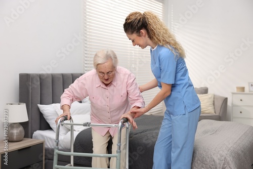 Cuadro en lienzo Care worker helping senior woman with walker to stand up from bed indoors