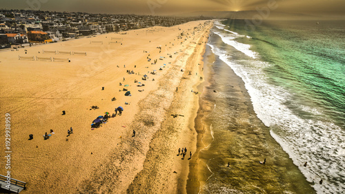 High-angle aerial view of Manhattan Beach at golden hour sunset with crowds and waves