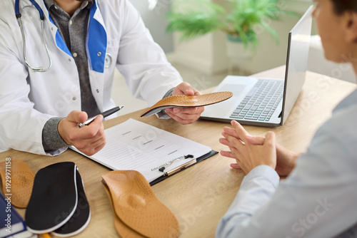 Orthopedist doctor shows orthopedic insoles to patient in medical clinic. They discuss custom orthotics and arch support to relieve foot pain. Concept medicine, foot healthcare and comfort.