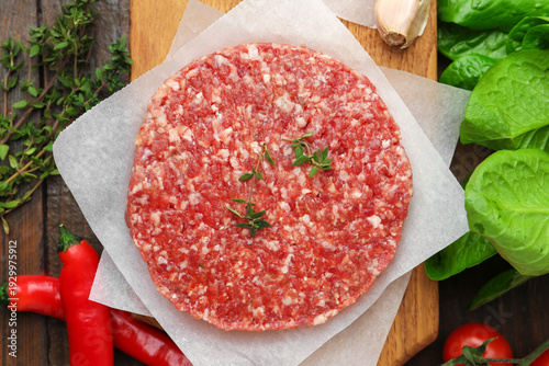 Uncooked meat patty with spices, tomatoes and lettuce on table, flat lay