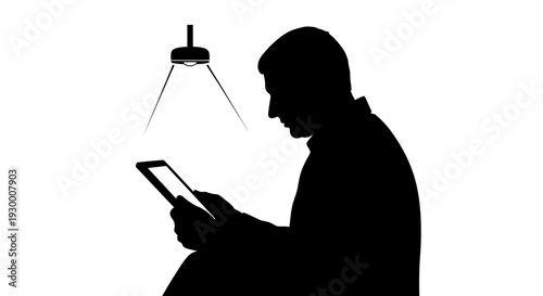Silhouette of a man sitting and using a tablet under a lamp.