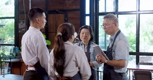 Asian senior restaurant owners stand with employees, teamwork meeting strengthens collaboration, leadership guidance creates positive energy, preparing small business team for successful service day