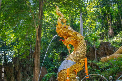 Golden Naga statue in tropical forest at Wat Prangkasi, Thong Pha Phum, Kanchanaburi, Thailand surrounded by lush green cliff landscape