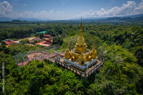 Aerial drone view of golden pagoda at Wat Prangkasi in Thong Pha Phum, Kanchanaburi, Thailand surrounded by lush forest mountain landscape